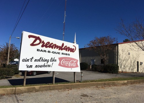 Sign for Dreamland Bar-B-Que Ribs with a slogan about their unique offerings, set against a clear blue sky.