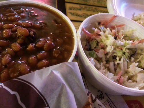 A bowl of baked beans next to a bowl of coleslaw on a table.