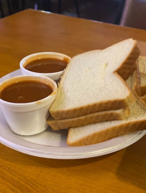 A plate with slices of white bread and two small cups of red sauce.