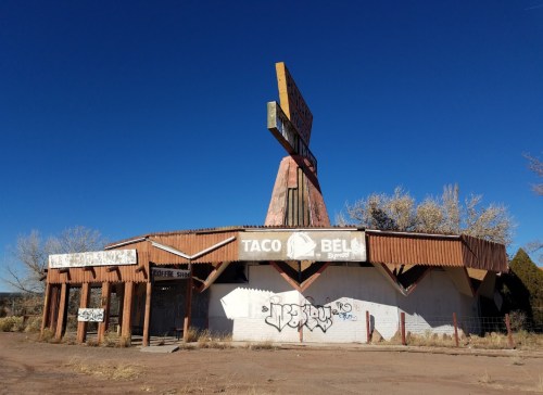 Abandoned Taco Bell building with graffiti, featuring a large sign and a clear blue sky in the background.
