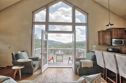 Cozy interior with large windows, mountain view, and a deck. Two chairs and a table create a welcoming atmosphere.