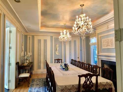 Elegant dining room with a long table, chandeliers, and decorative walls, featuring a floral centerpiece.