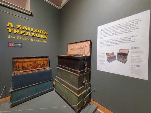 Three antique sea chests displayed against a green wall, with an informational panel about sailors' treasures nearby.