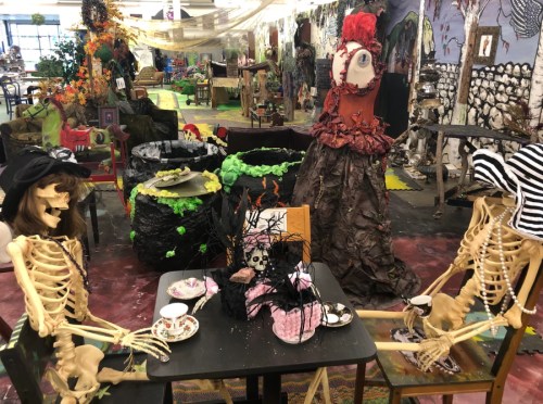 Two skeletons sit at a table with Halloween decorations, surrounded by a whimsical, spooky-themed room.