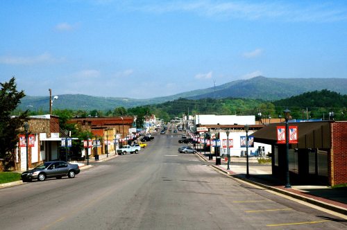 A view of a small town street lined with shops, cars, and mountains in the background under a clear blue sky.