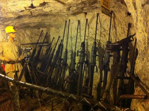 A dimly lit mine with a mannequin and a display of old mining tools and equipment against the rocky wall.