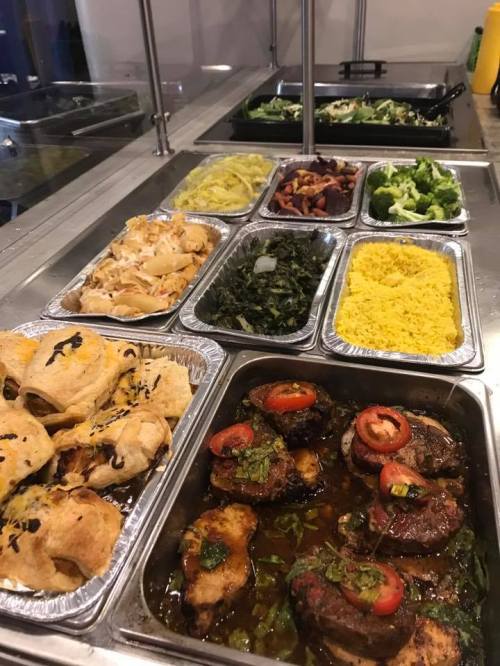 A buffet display featuring various dishes, including meats, rice, vegetables, and pastries in metal trays.