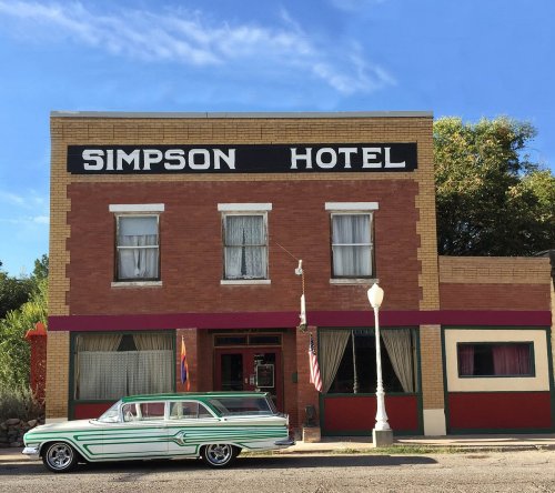 Historic Simpson Hotel building with a classic green and white car parked in front under a clear blue sky.