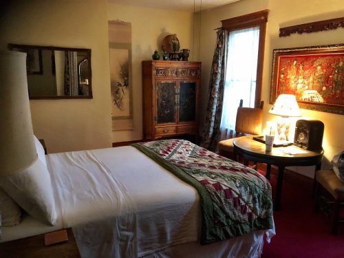 Cozy bedroom with a bed, quilt, wooden furniture, a lamp, and decorative artwork on the walls.
