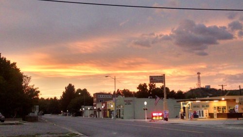 A quiet street at sunset, with colorful clouds and small shops lining the road, creating a serene atmosphere.