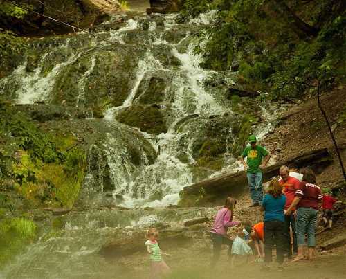 A group of people gathers by a cascading waterfall, enjoying nature and playing near the water's edge.