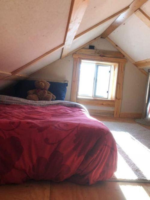 Cozy attic bedroom with a bed, teddy bear, and a small window letting in natural light.