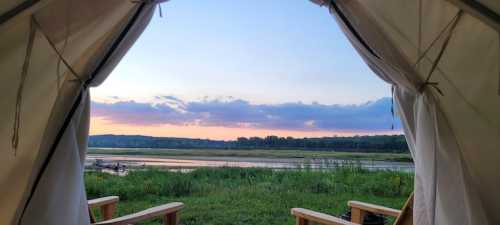 View from a tent opening, showcasing a serene river landscape at sunset with colorful clouds and green grass.