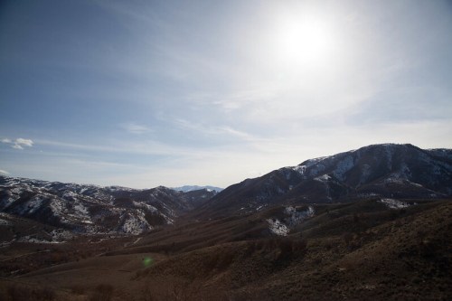A panoramic view of snow-capped mountains under a bright sun and clear blue sky.