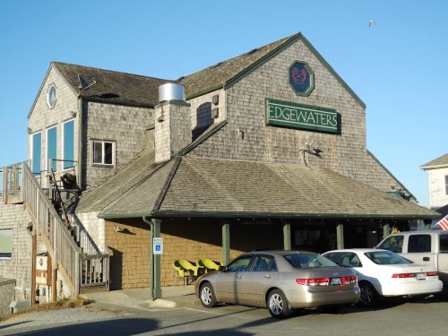 A rustic building with a sign reading "Edgewaters," featuring a sloped roof and parked cars in front.