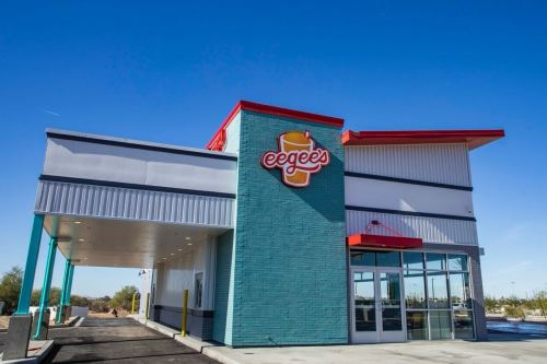 A colorful fast-food restaurant with a drive-thru, featuring a large sign that reads "eegees." Clear blue sky in the background.