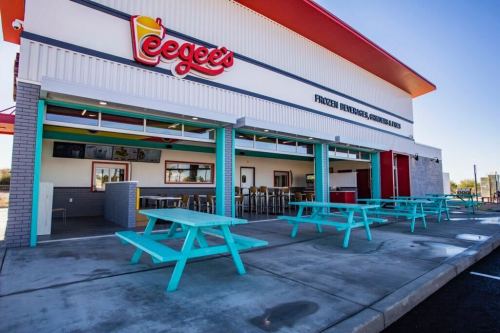 Exterior of a colorful eatery with turquoise picnic tables and a sign reading "Eegee's," featuring a bright, sunny sky.