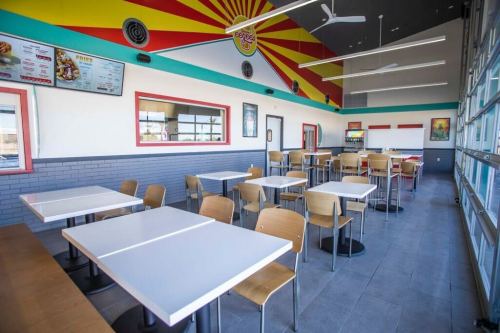 Brightly colored restaurant interior with empty tables and chairs, featuring a menu board and large windows.