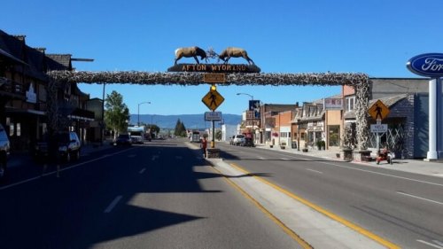 A street view of Afton, Wyoming, featuring a decorative arch with two moose and shops lining the road.