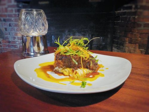 A beautifully plated dish featuring meat topped with fresh herbs and orange zest, served on a white plate.