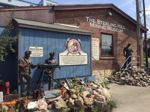 Exterior of the Sterling Hill Mining Museum, featuring mining-themed sculptures and a sign about the museum.