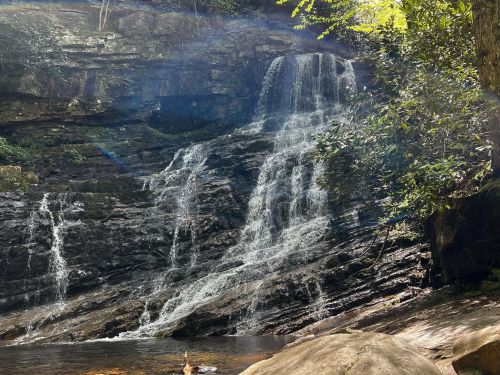 A serene waterfall cascading over rocky cliffs, surrounded by lush greenery and sunlight filtering through the trees.