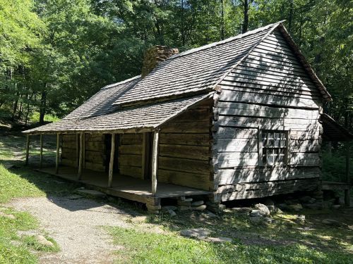 A rustic wooden cabin surrounded by trees, featuring a porch and a stone chimney.