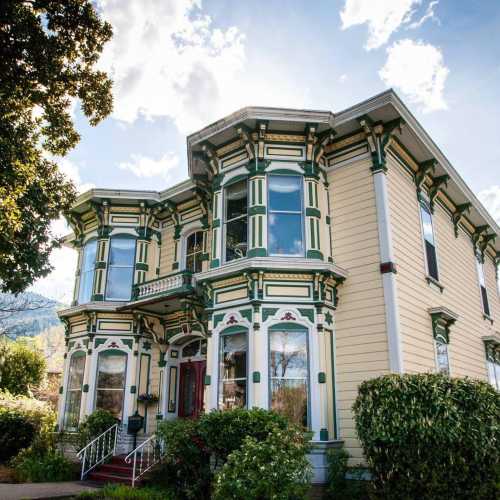 A colorful Victorian-style house with intricate details, surrounded by greenery and a clear blue sky.