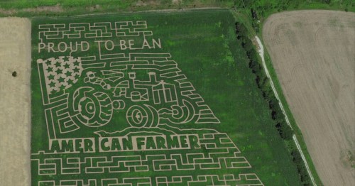 Aerial view of a corn maze featuring a tractor and the words "Proud to be an American Farmer" with an American flag design.