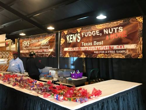 A vendor booth displaying "Ken's Fudge, Nuts & More" with colorful treats and a sign offering free samples.