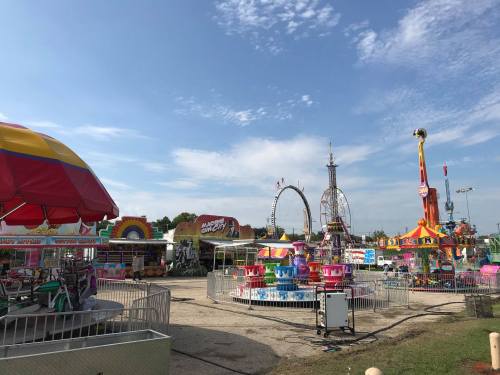 A colorful amusement park scene featuring rides, games, and a clear blue sky.