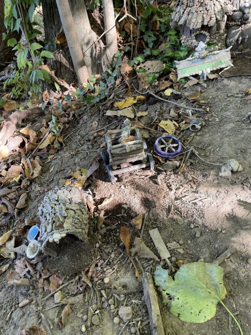 A whimsical miniature scene in a forest, featuring a small cart and natural materials among fallen leaves and dirt.