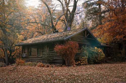 A cozy log cabin surrounded by vibrant autumn foliage and fallen leaves, set in a serene natural landscape.