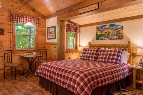 Cozy cabin interior featuring a plaid bedspread, wooden accents, and a small dining table by the window.