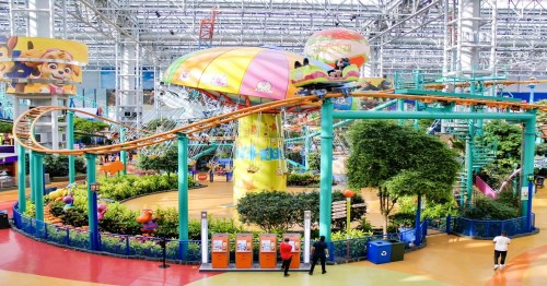 A colorful indoor amusement park with a roller coaster, vibrant decorations, and lush greenery.
