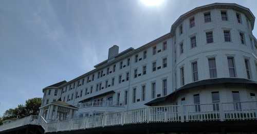 A large, white, multi-story building with a curved design, set against a clear sky and bright sun.