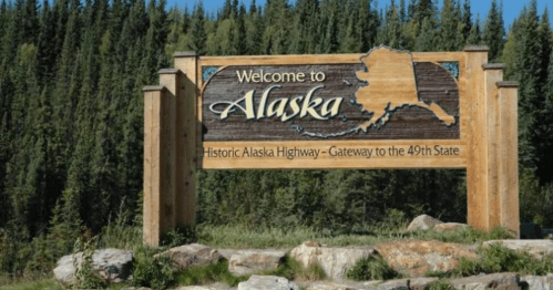 Wooden welcome sign for Alaska, featuring the state outline and text about the historic Alaska Highway.
