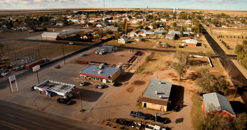 Aerial view of a small town with residential areas, roads, and a gas station, surrounded by open land.