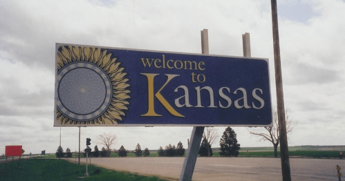 A welcome sign for Kansas featuring a sunflower design against a cloudy sky.