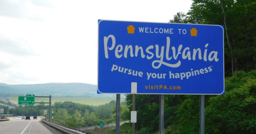 Welcome sign for Pennsylvania with the slogan "pursue your happiness" and scenic hills in the background.