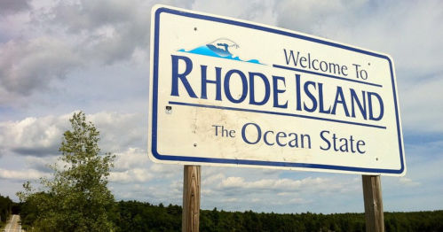 Welcome sign for Rhode Island, labeled "The Ocean State," with a blue sky and trees in the background.