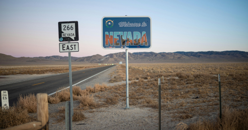 A welcome sign for Nevada along a deserted road, with mountains in the background and a clear sky at dusk.