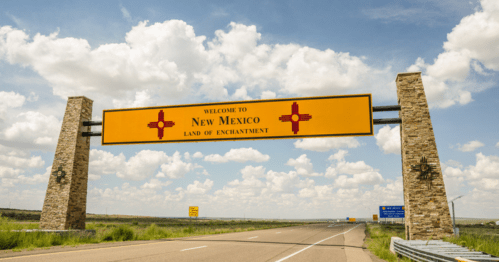 Welcome sign for New Mexico, featuring "Land of Enchantment" against a backdrop of blue skies and clouds.