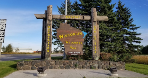 Welcome sign for Wisconsin featuring wooden structure and text highlighting industry, recreation, and agriculture.