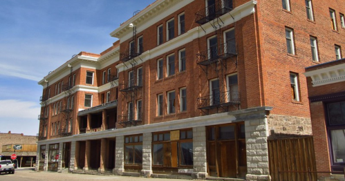 Historic brick building with multiple stories and fire escapes, set against a blue sky.