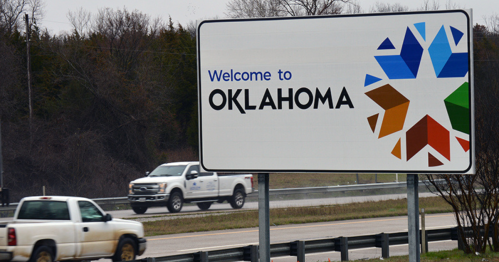 Sign welcoming travelers to Oklahoma, featuring colorful geometric designs and a highway in the foreground.