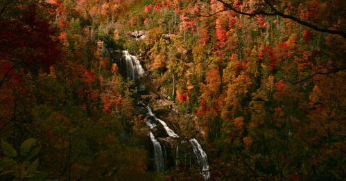 A scenic waterfall surrounded by vibrant autumn foliage in shades of orange, red, and yellow.