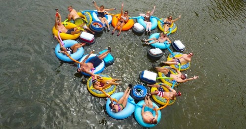 A group of people floating in colorful inner tubes, forming a circle on a river, enjoying a sunny day.