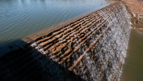 A cascading waterfall flows over a textured stone surface into a calm body of water below.