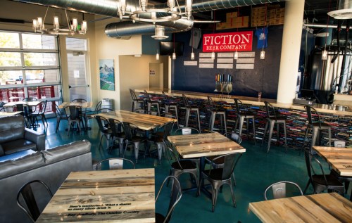 Interior of Fiction Beer Company featuring wooden tables, a bar with taps, and a modern industrial design.